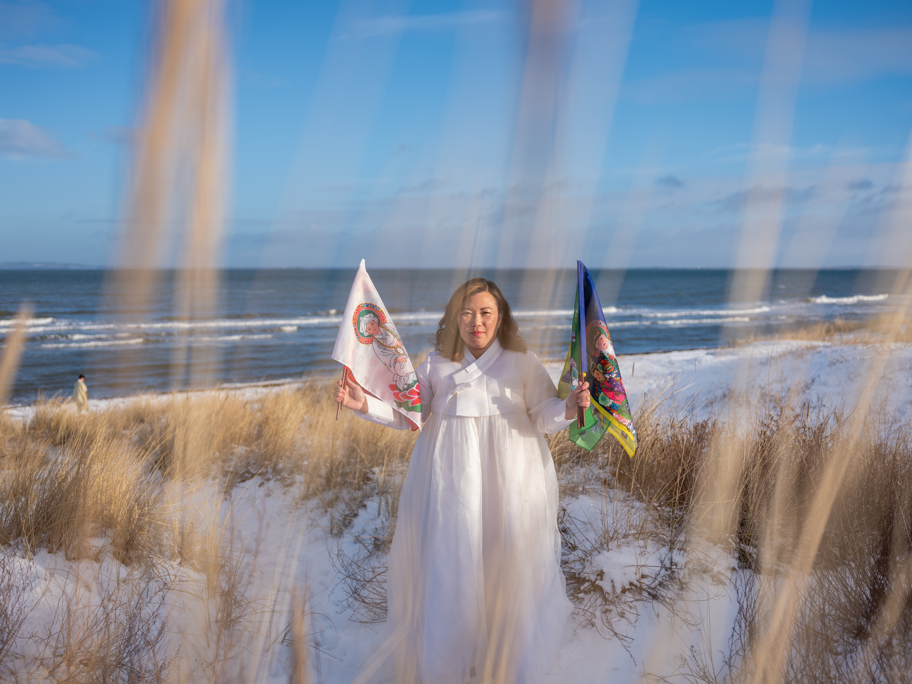 caption: <em>Helena Soholm holds up the five directional flags of Korean shamanism in Dronningmølle, Denmark.</em>