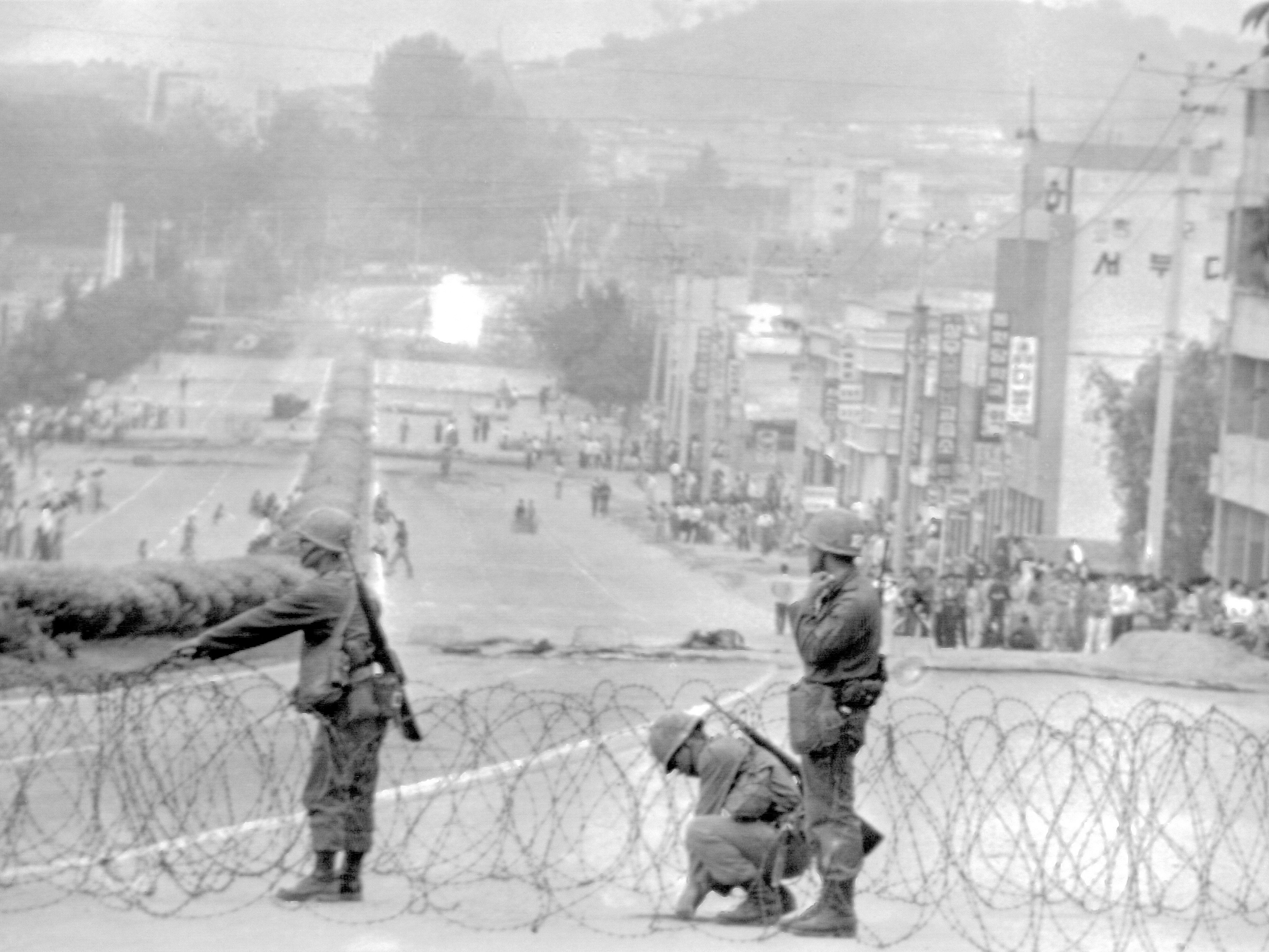 caption: Government soldiers erect a roadblock on a street leading to downtown Gwangju, South Korea, with citizens looking on, on May 26, 1980.