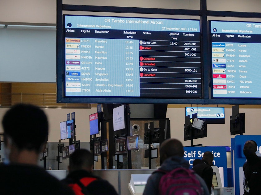 caption: Travelers walk near an electronic flight notice board displaying canceled flights at O.R. Tambo International Airport in Johannesburg, South Africa, on Saturday. Several countries have begun travel bans in response to the omicron variant.