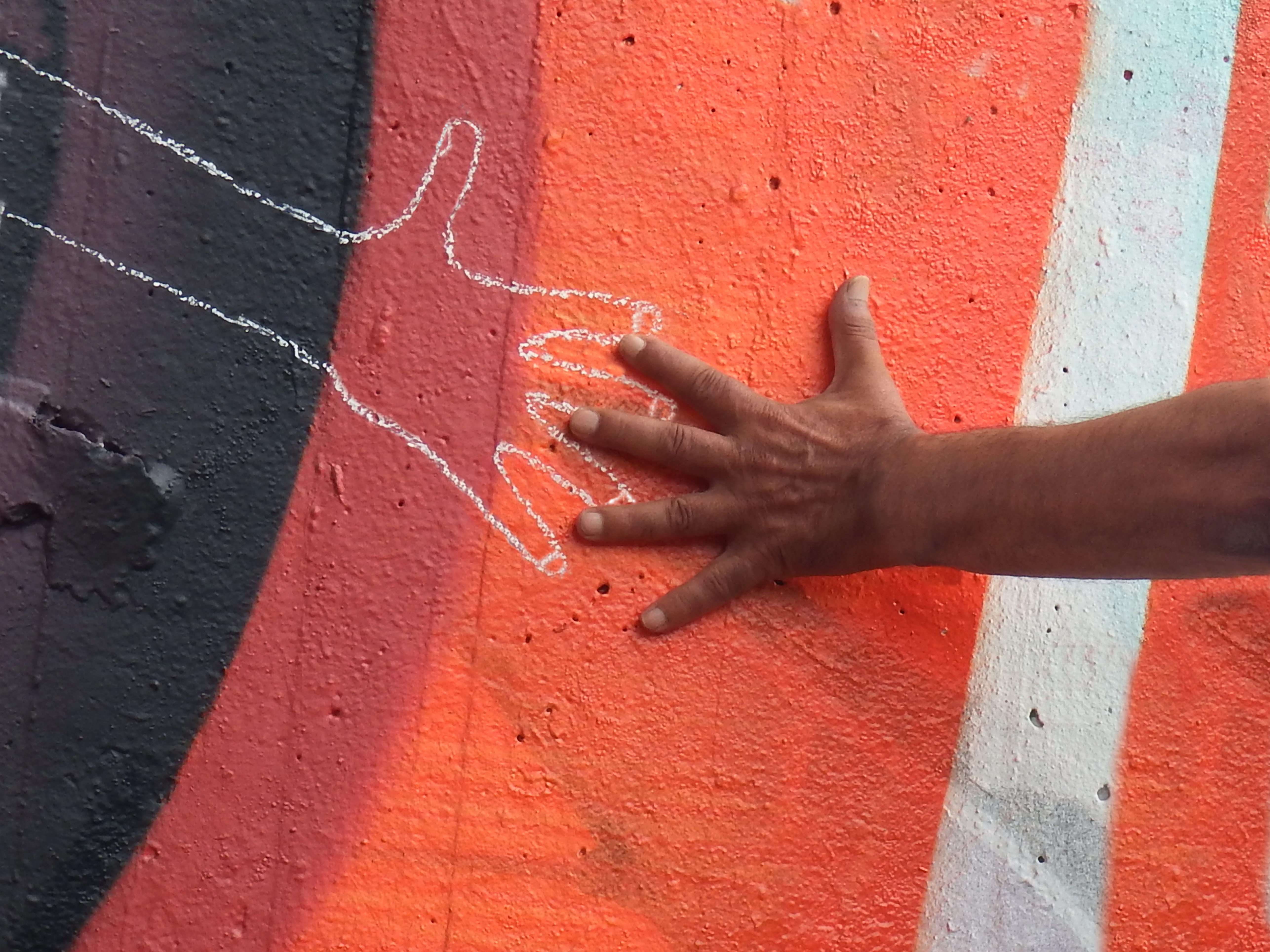 A child's hand extends out to a chalk lining of a hand drawn on a wall.