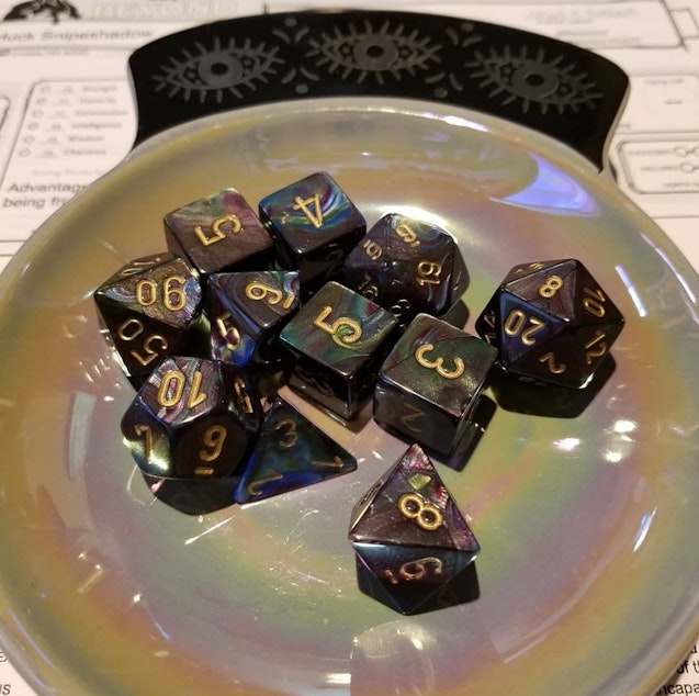 caption: A dish with a standard 11 dice set on top of a D&D character sheet.