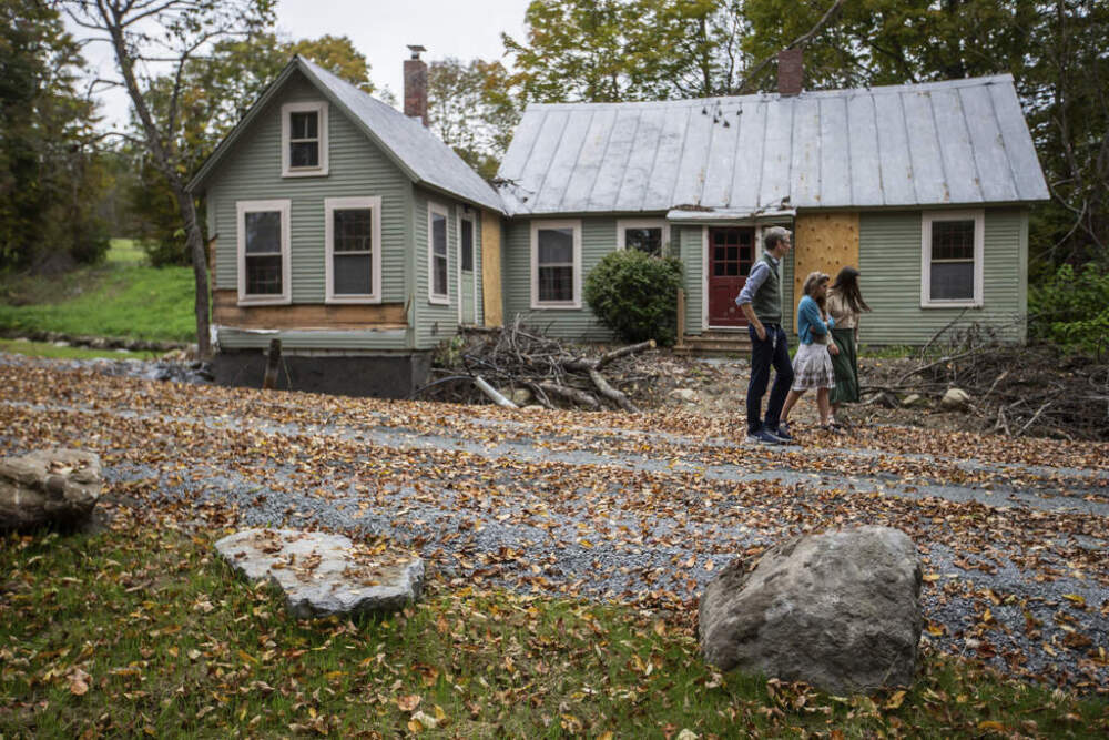 caption: John, left, Jenny and Lila, right, Mackenzie walk around their flood-damaged property in Peachman, Vt. on Sept. 23, 2024. (AP Photo/Dmitri Beliakov)