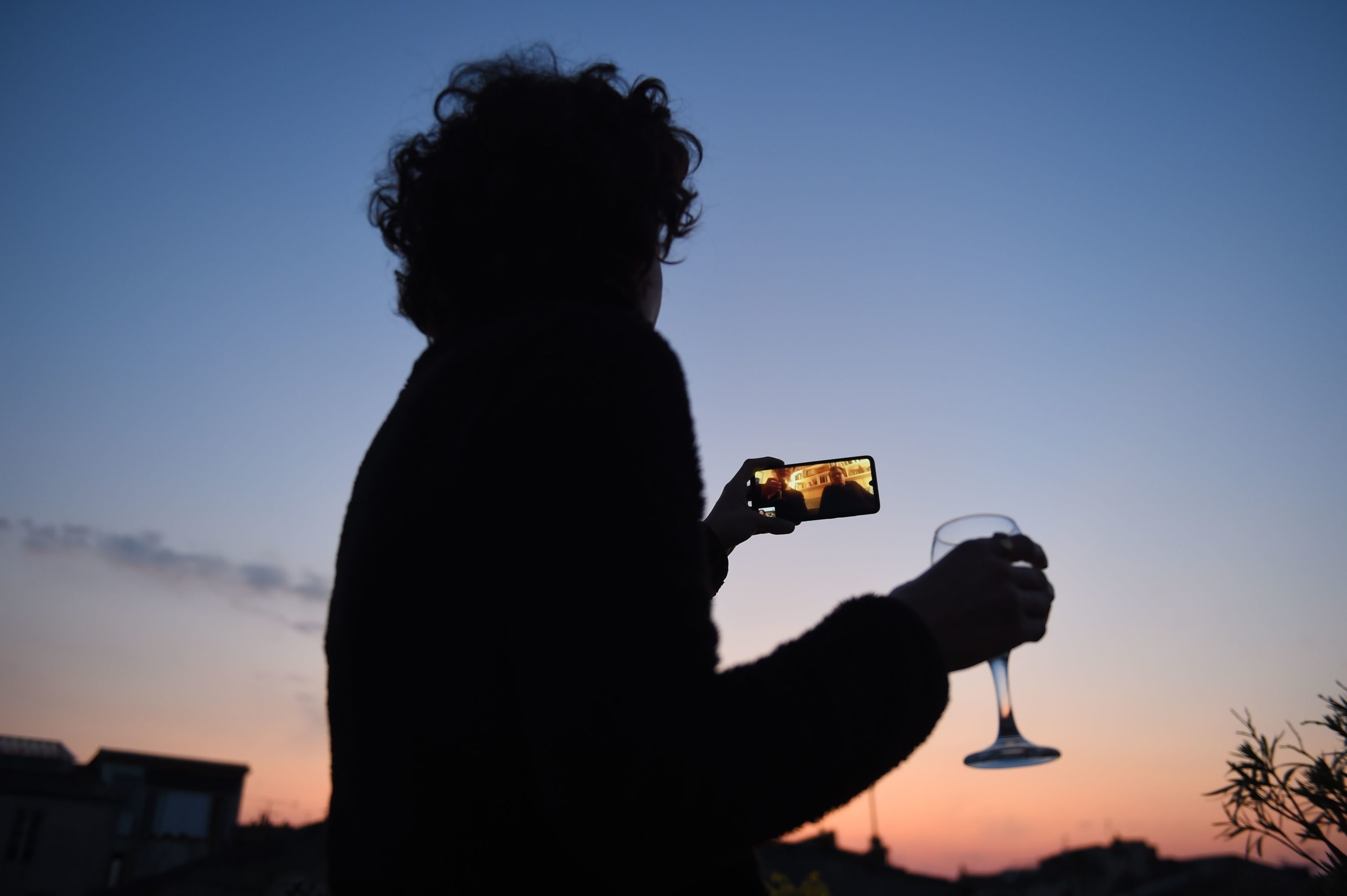 caption: A woman drinks a glass of wine as she speaks and shares a drink with friends via a video call on March 26, 2020, in Bordeaux, southwestern France, in the evening on the tenth day of a lockdown aimed at curbing the spread of the COVID-19 (novel coronavirus) in France. (NICOLAS TUCAT/AFP via Getty Images)