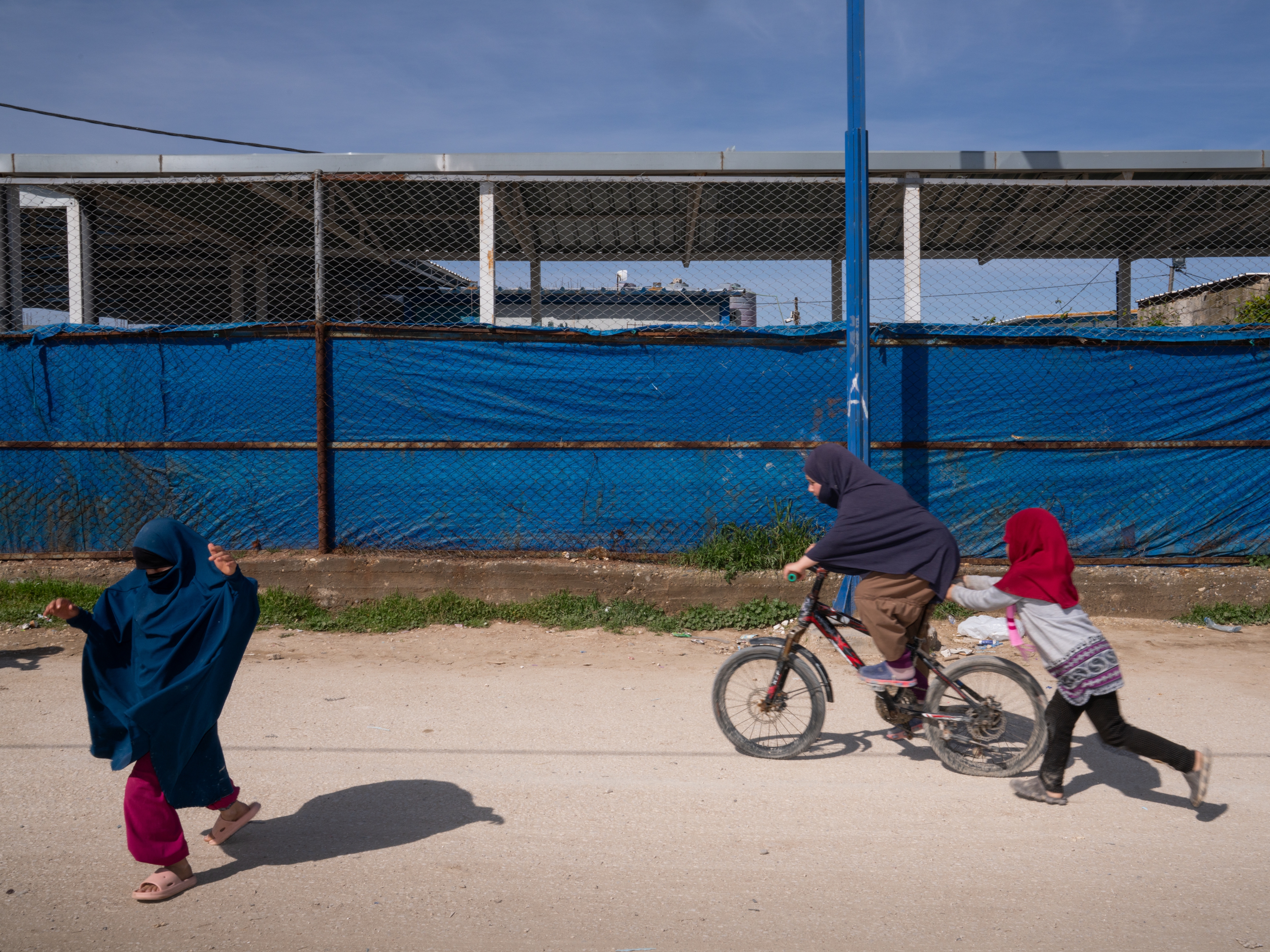 caption: Children ride a bicycle and play in the Roj camp in a Kurdish-held territory in northeast Syria in March. The detention camp houses wives and children of ISIS members.