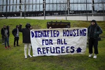 caption: "Dignified Housing for All Refugees" reads a banner as asylum seekers once housed at the Sleep Inn in SeaTac march to Seattle City Hall along with activists, mutual aid organizations and allies to ask for assistance with housing from Seattle city councilmembers on Tuesday, February 27, 2024, in Seattle. 