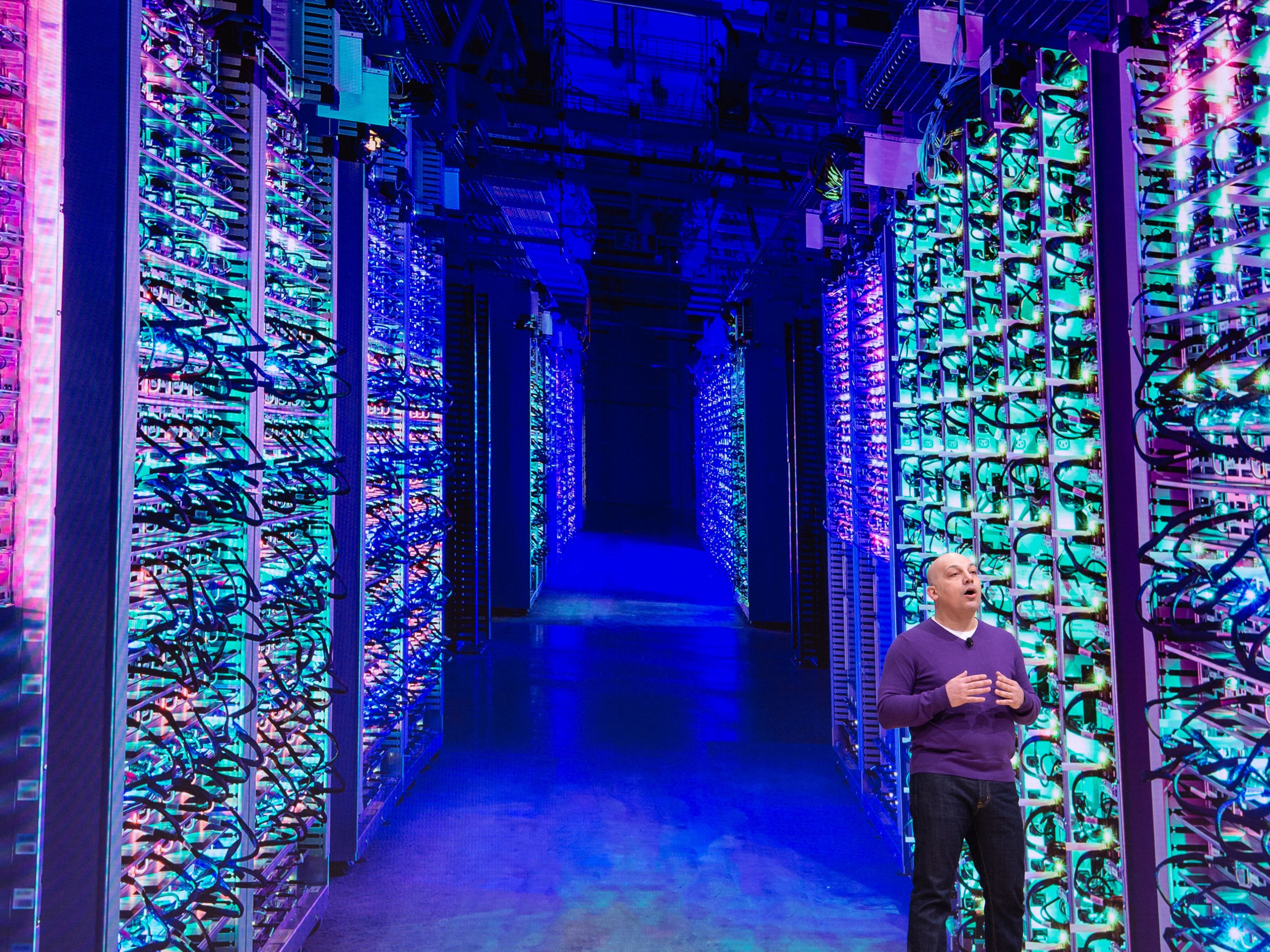 caption: Google Vice President Majd Bakar speaks on-stage during an annual conference in San Francisco with the back drop of a massive data center.
