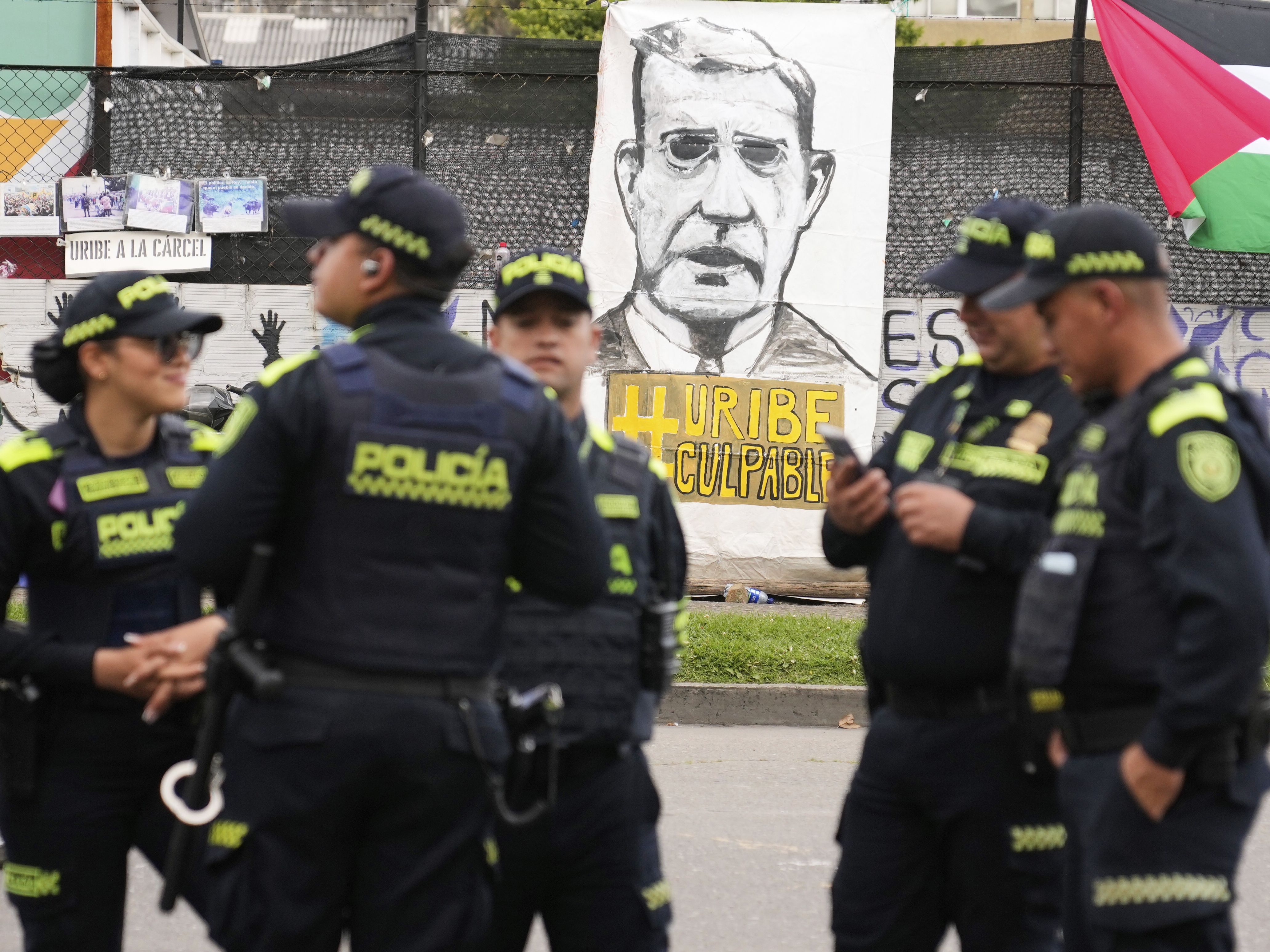 caption: Police stand in front of a banner reading in Spanish "Uribe guilty" displayed by opponents of former President Alvaro Uribe outside the court where a verdict is expected in his trial for witness tampering in Bogota, Colombia, on July 28, 2025.