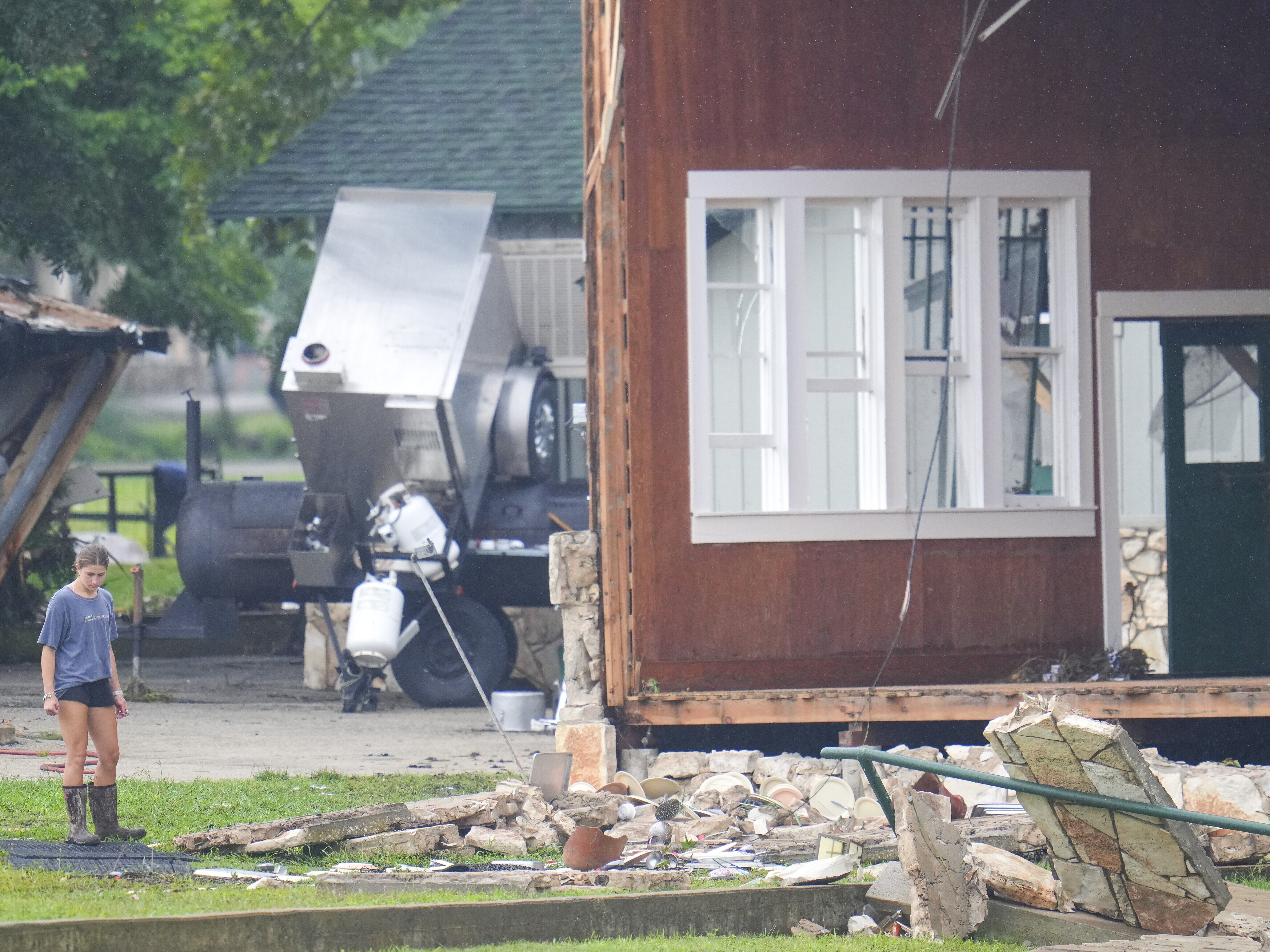 caption: A person looks at damage to the main building at Camp Mystic, along the banks of the Guadalupe River in Texas. A flash flood swept through the area in the early hours of July 4, 2025. Climate change is making heavy rain more common, leading to more flood risk in much of the U.S.