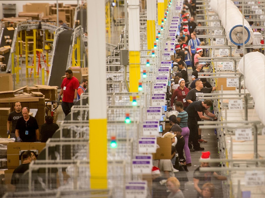 caption: Amazon says it will pay all its U.S. workers at least $15. Here, workers prepare shipments at an Amazon Fulfillment Center in California during the early Christmas rush in 2014.