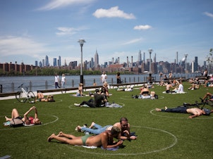 caption: People sit inside social distancing markers at the Domino Park in Brooklyn borough of New York on May 27, 2020. Stay-at-home orders in New York helped to lower the state's reproduction number, which estimates how many people one sick person could infect with the coronavirus.