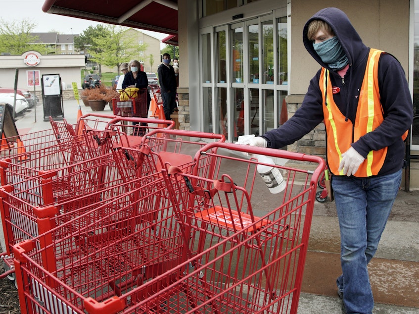 caption: A Trader Joe's worker disinfects shopping carts and controls the number of customers allowed to shop at one time in Omaha, Neb., on May 7, 2020. Grocers like Trader Joe's are offering pay incentives to encourage their workers to get vaccinated against COVID-19.