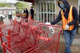 caption: A Trader Joe's worker disinfects shopping carts and controls the number of customers allowed to shop at one time in Omaha, Neb., on May 7, 2020. Grocers like Trader Joe's are offering pay incentives to encourage their workers to get vaccinated against COVID-19.