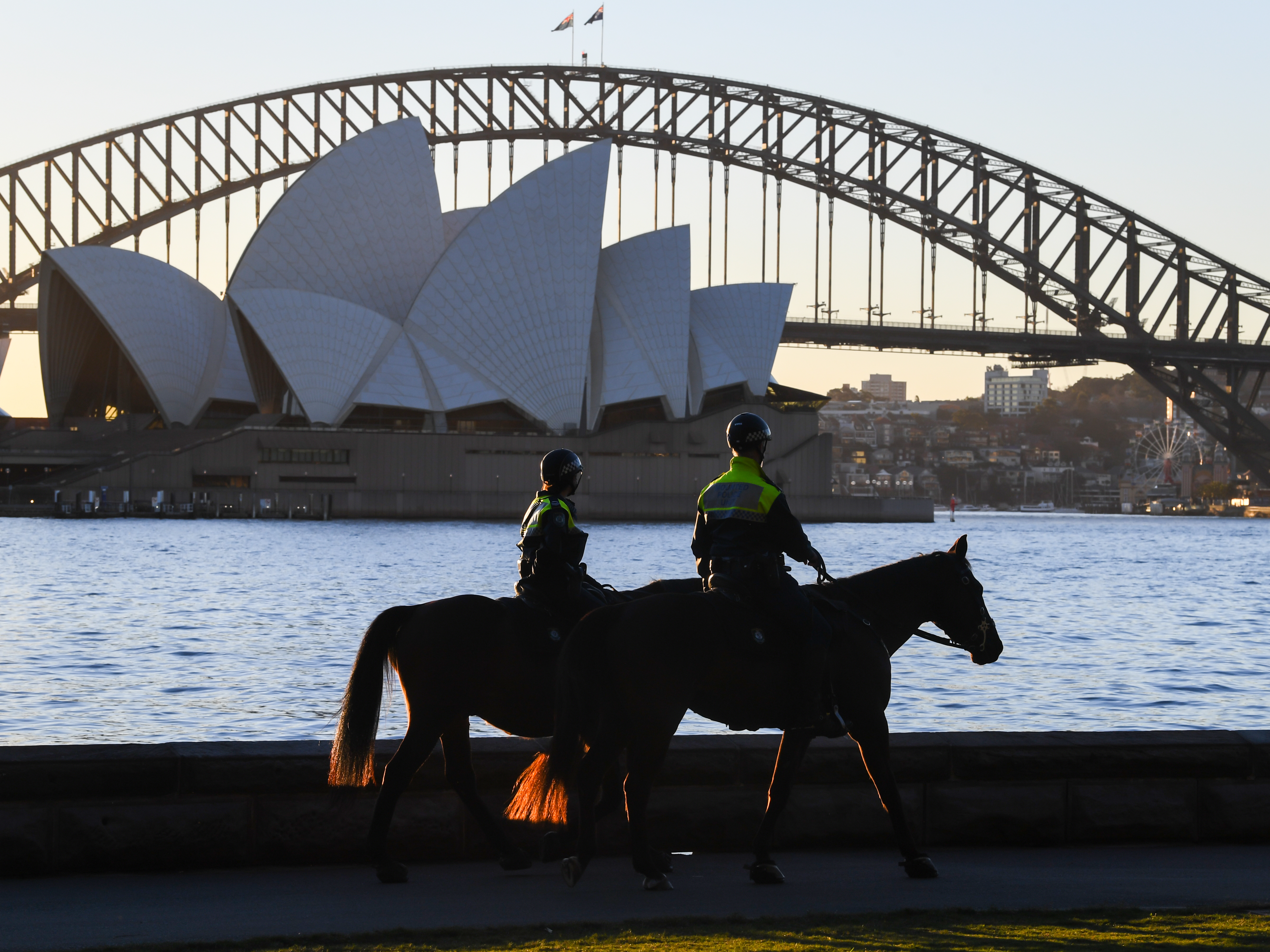 caption: Mounted police officers patrol around the edge of Sydney Harbor on Friday as the Australian city has been locked down amid a new surge in coronavirus infections.