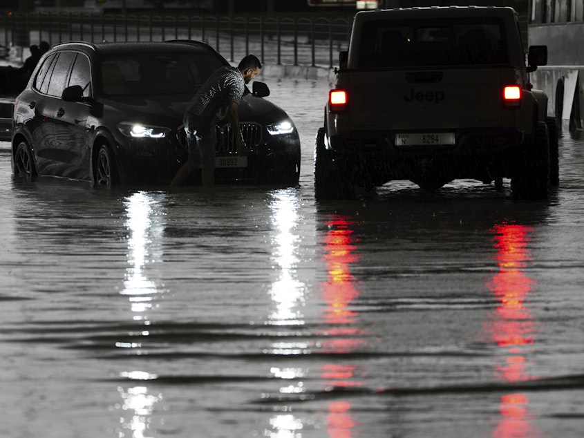 caption: A man tries to work on his stalled SUV in standing water in Dubai, United Arab Emirates, on Tuesday.
