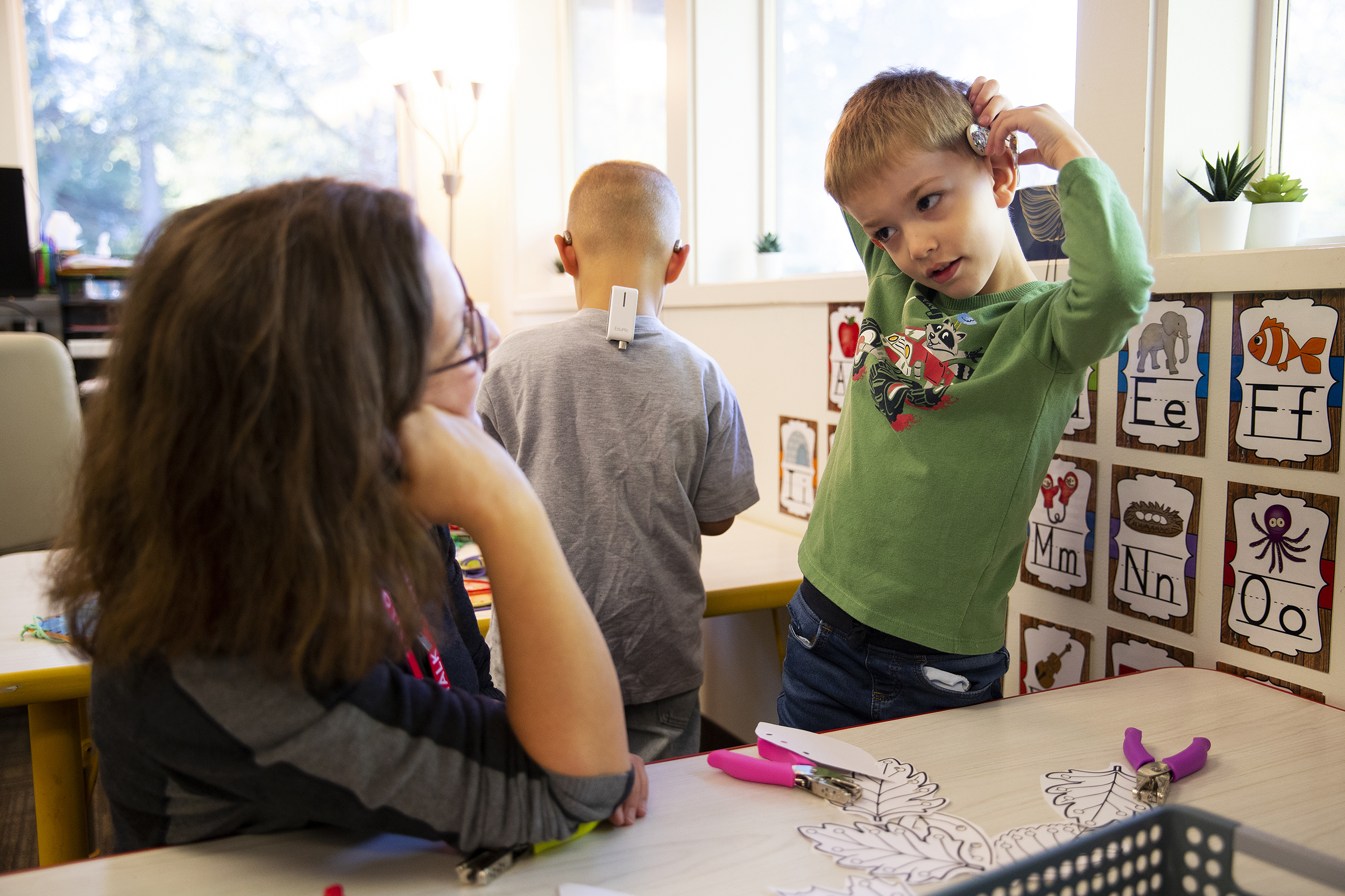 caption: Mona Oster, education and research director at Listen and Talk, assists a 4-year-old student as they practice putting on cochlear implants by themselves, on Tuesday, October 14, 2025, in Kirkland. 