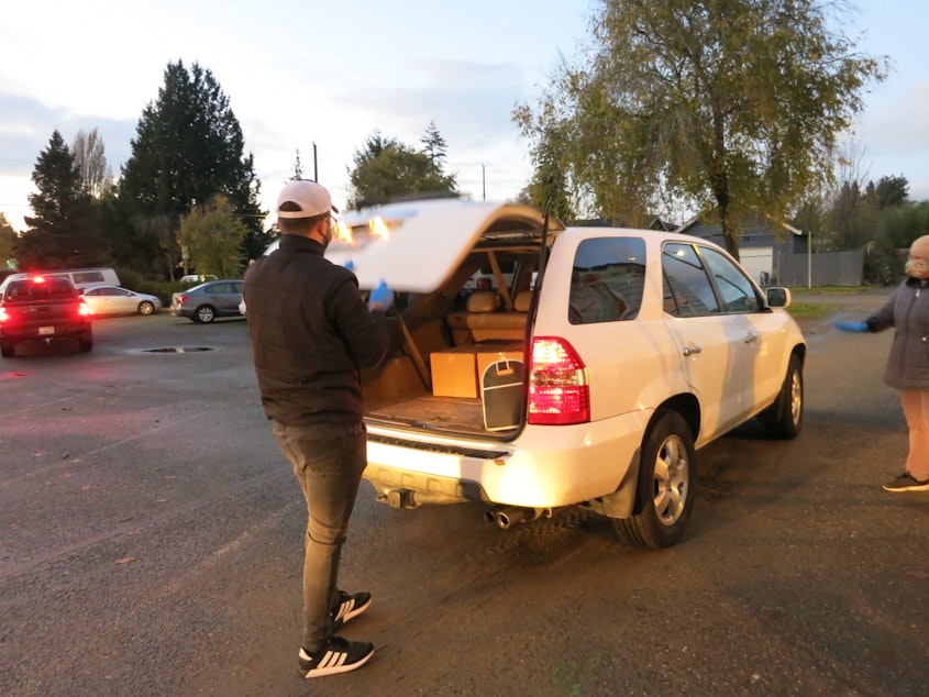 caption: A volunteer at El Dios Viviente church in White Center loads a car with donated food at the church's biweekly distribution event. 