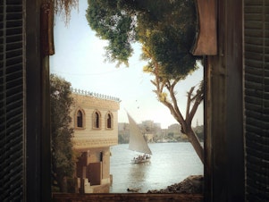 caption: El Massry took this photo of a felucca sailing down the Nile in the south of Cairo on a morning in 2022. He digitally framed the image with a photo of a window in an old antique shop, and in his signature style, added a bird or two.