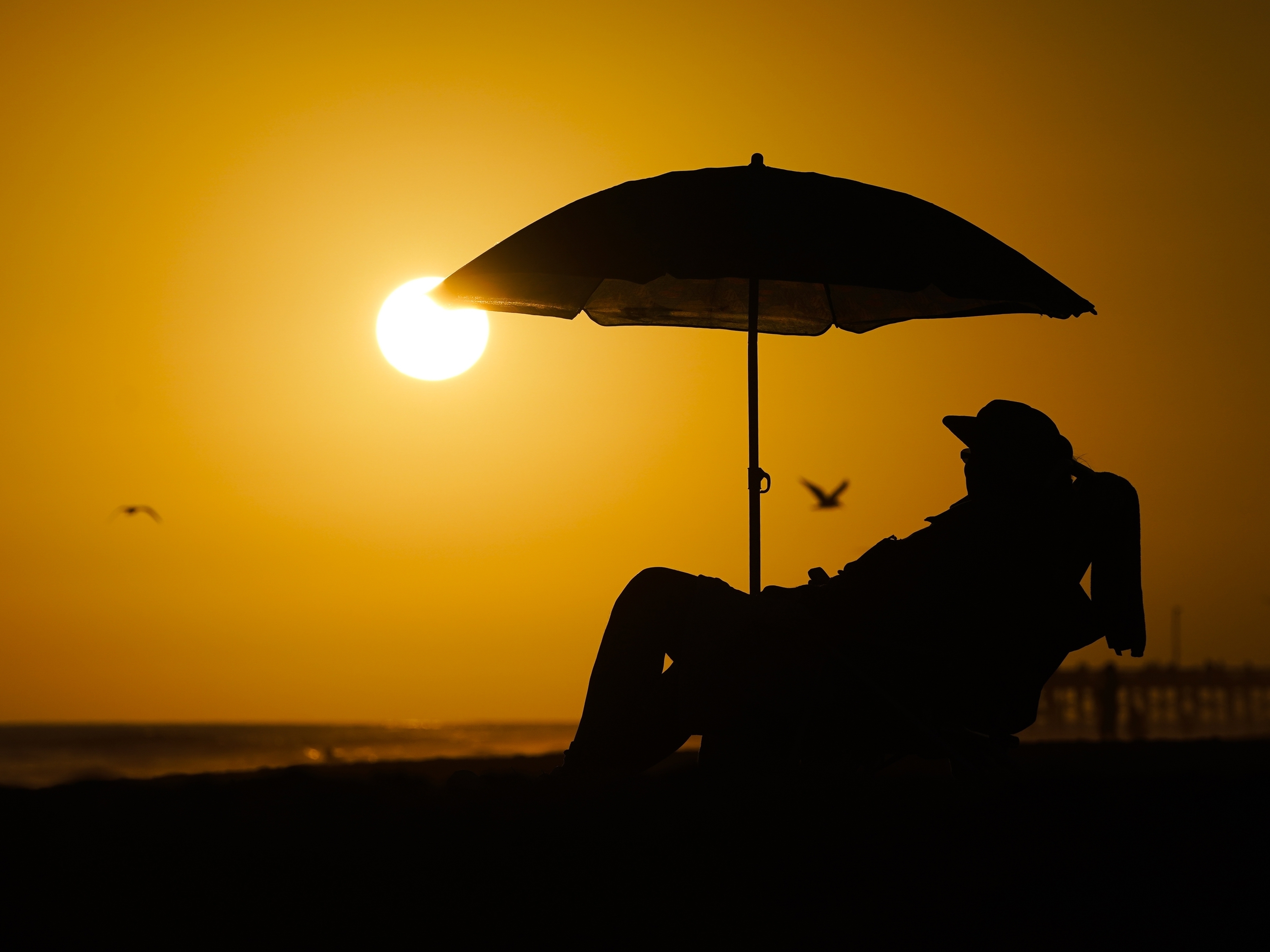 caption: A person rests under an umbrella as the sun sets, Sept. 12, 2023, in Newport Beach, Calif. After a summer of record-smashing heat, warming somehow got even worse in September as Earth set a new mark for how far above normal temperatures were, the European climate agency reported.