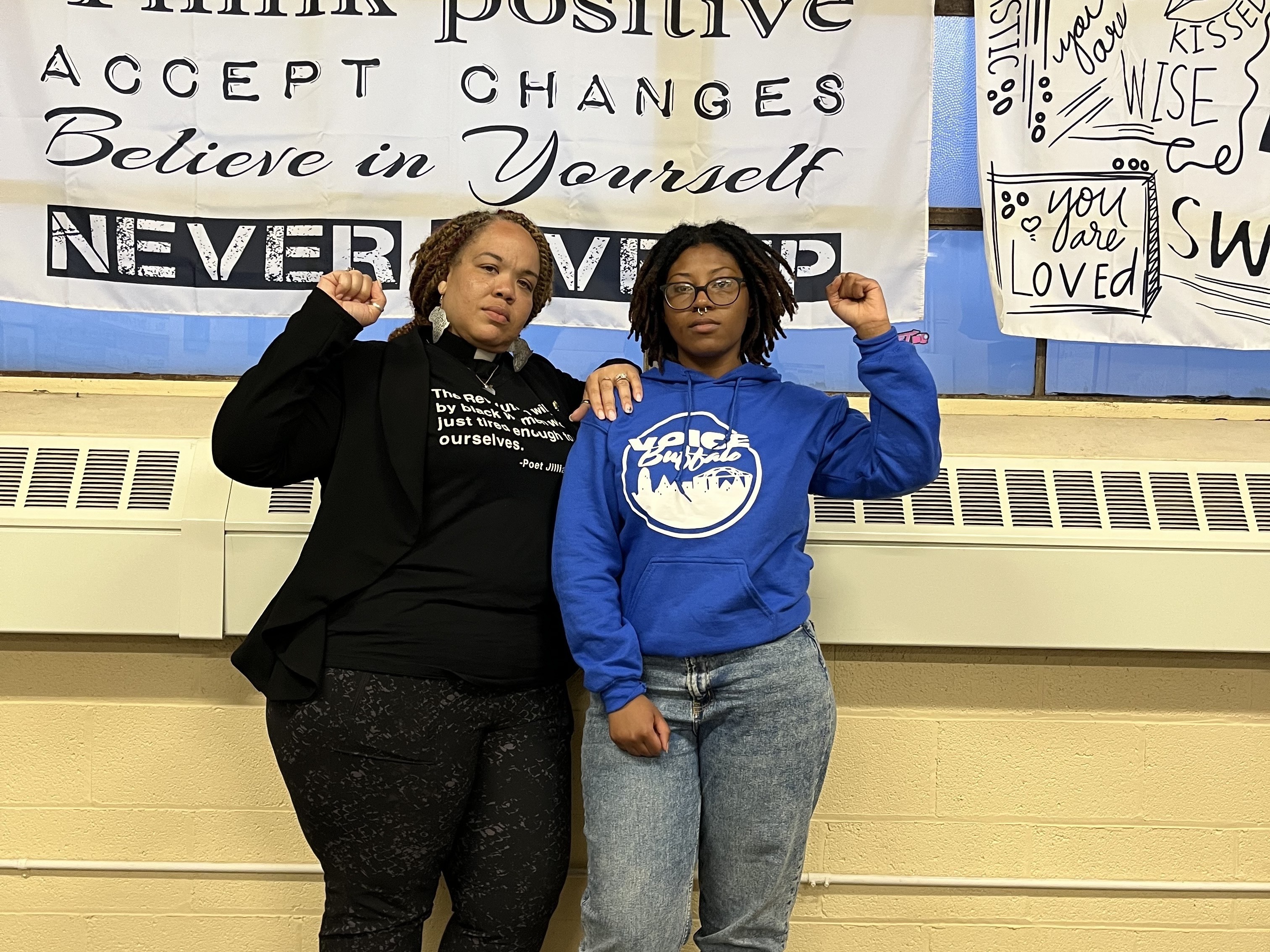 caption: Rev. Denise O. Walden-Glenn and Alia Williams each raise a fist— a symbol of solidarity and Black power— at the VOICE office in Buffalo, New York.