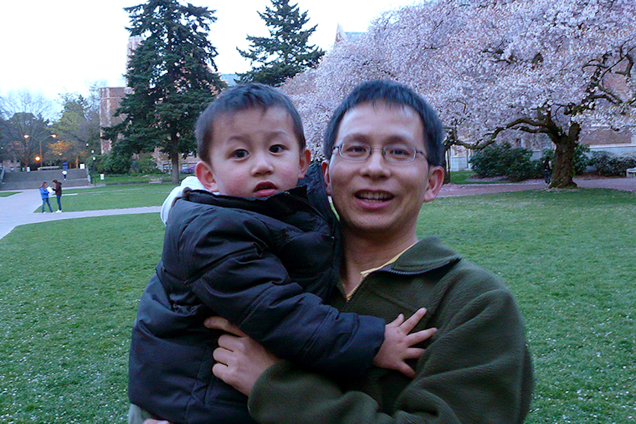 caption: Weibin Zhou (right) holding his child Phillip Zhou in front of the cherry blossom trees on the University of Washington campus in the early 2010s. 