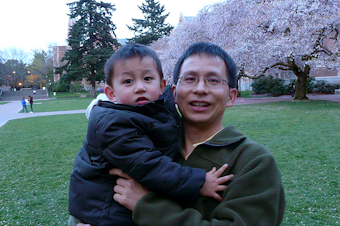caption: Weibin Zhou (right) holding his child Phillip Zhou in front of the cherry blossom trees on the University of Washington campus in the early 2010s. 