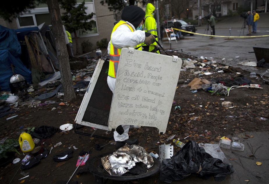caption: A Seattle Parks and Recreation employee discards a hand written sign that was left behind after unhoused community members were swept from the Ballard Commons Park on Tuesday, December 7, 2021, in Seattle. 