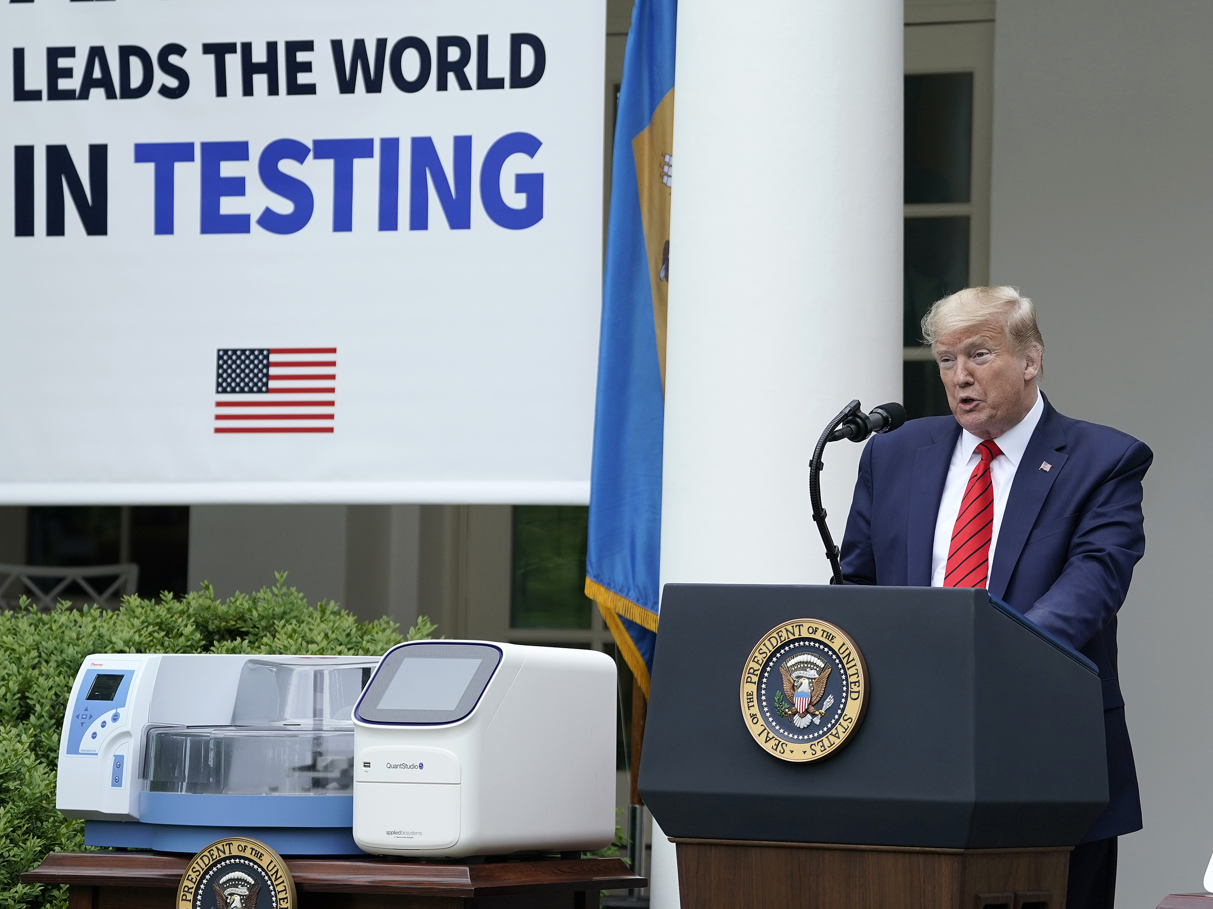 caption: President Donald Trump, flanked by tables holding testing supplies and machines, speaks during a press briefing about coronavirus testing in the Rose Garden of the White House on May 11, 2020 in Washington, D.C.