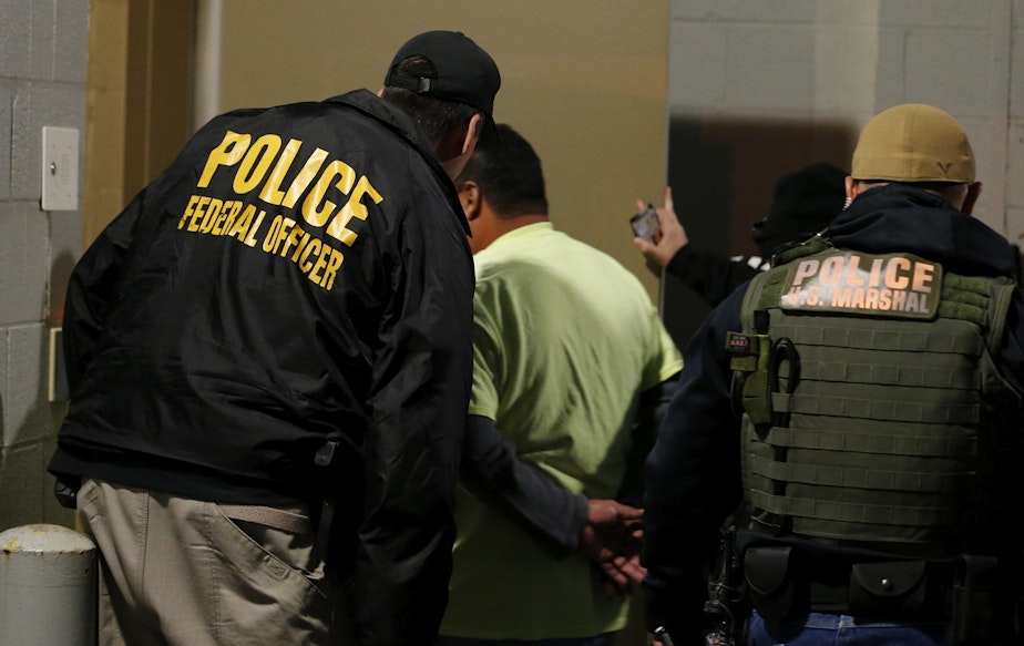 caption: FILE - In this Oct. 22, 2018, file photo U.S. Immigration and Customs Enforcement agents escort a target to lockup during a raid in Richmond, Va. Carrying out President Donald Trump's hard-line immigration policies has exposed ICE to unprecedented public scrutiny and criticism, even though officers say they're doing largely the same job they did before the election, prioritizing criminals. 