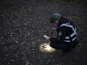 caption: A Ukrainian police officer uses a flashlight to search for drone debris near the site of an explosion following a Russian drone attack in Kyiv, Ukraine, on Saturday, Nov. 25, 2023, its most intense on the Ukrainian capital since the beginning of its invasion, military officials said.