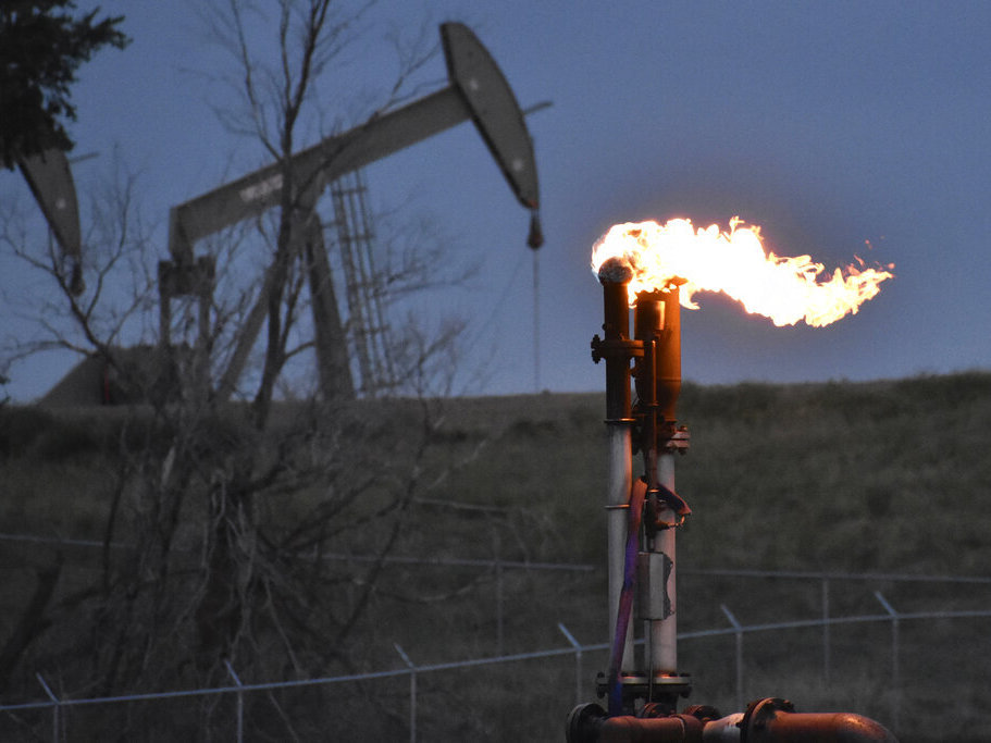 caption: A flare to burn methane from oil production is seen in August 2021 on a well pad near Watford City, N.D.