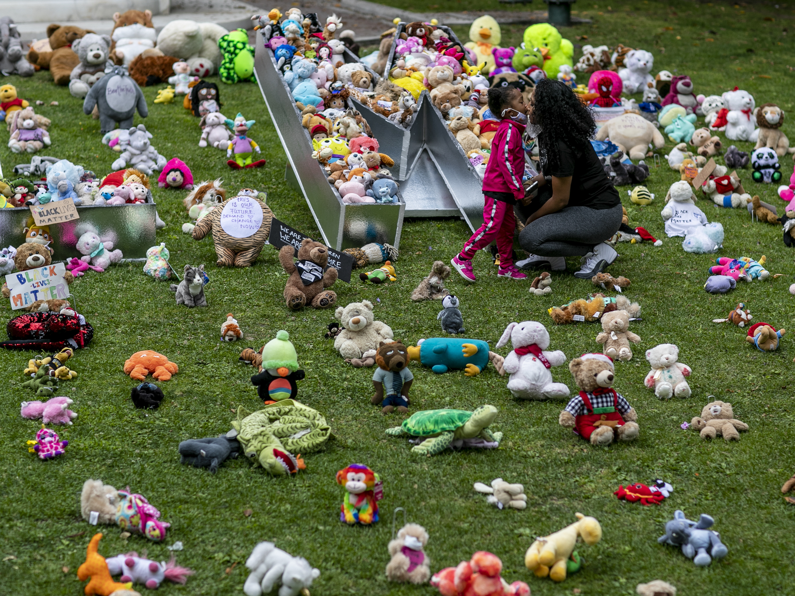 caption: A young girl and her mother visit a temporary art installation, called Bear the Truth, on June 28, 2020, at the Los Angeles City Hall. The installation honors Black children who have lost their lives to racial injustice and senseless violence.