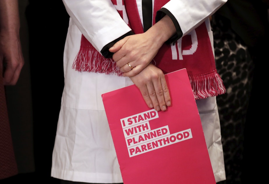 caption: FILE - In this, Feb. 25, 2019, file photo, Dr. Erin Berry, Washington State Medical Director for Planned Parenthood of the Great Northwest and the Hawaiian Islands, holds a folder as she listens at a news conference announcing a lawsuit challenging the Trump administration's Title X "gag rule" in Seattle.