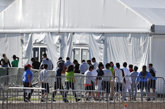 caption: Migrant children line up to enter a tent at the Homestead Temporary Shelter for Unaccompanied Children in Homestead, Fla. in February 2019.