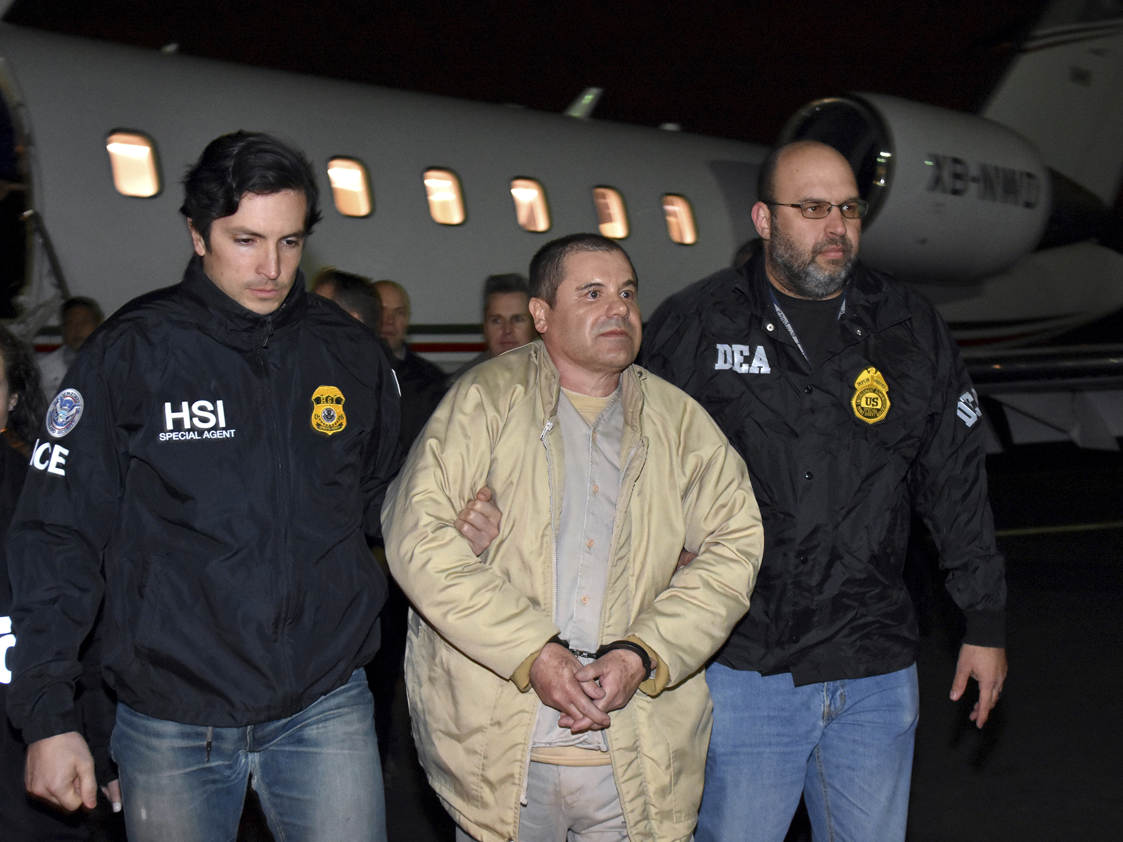 caption: U.S. law enforcement personnel escort Joaquín "El Chapo" Guzmán from a plane to a waiting caravan of SUVs at New York's Long Island MacArthur Airport in January 2017.