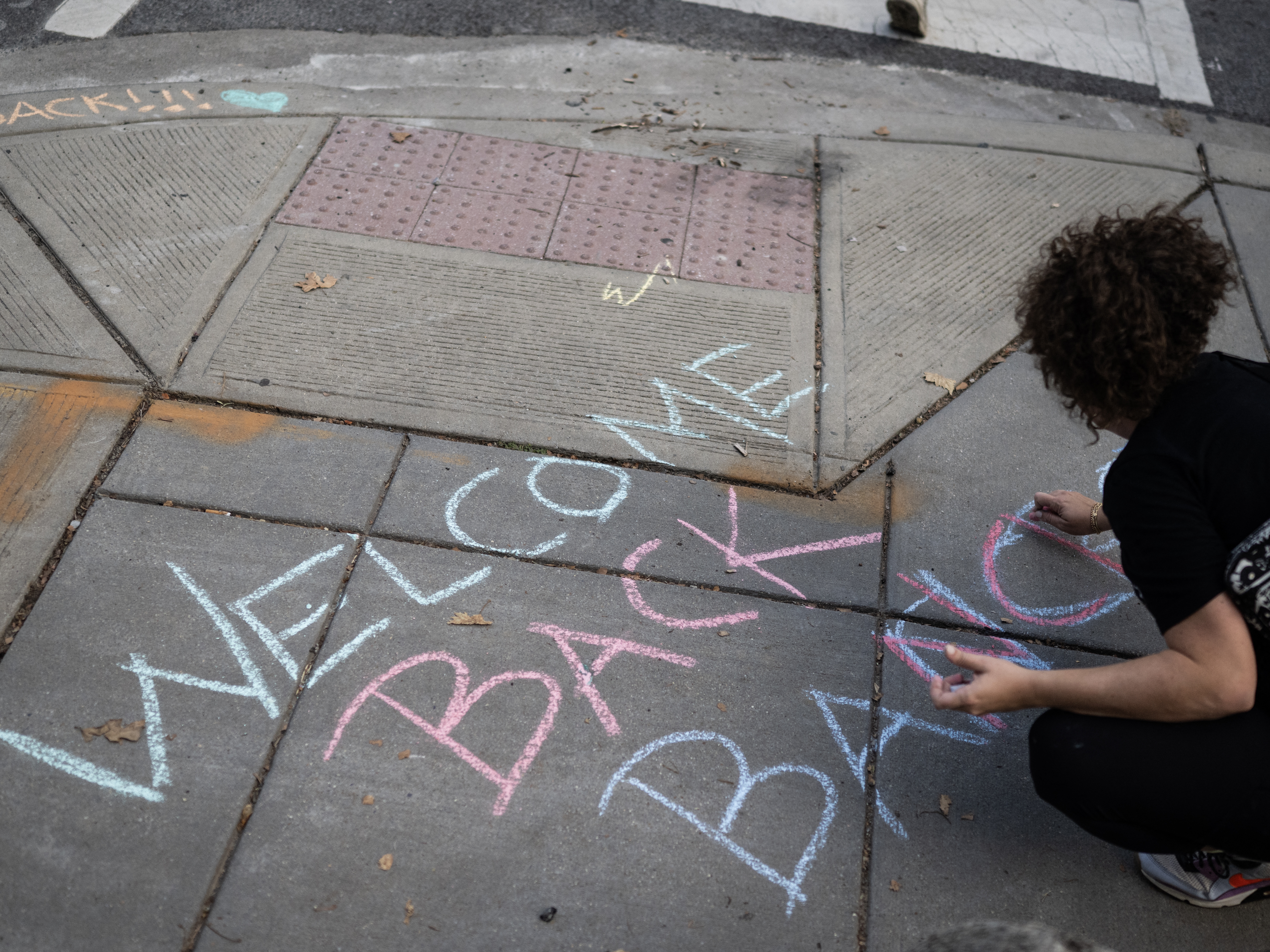 caption: A member of the community writes a welcome back note for students on the first day of DC Public Schools outside an elementary in Washington, DC on August 25, 2025, as a show of support as Immigration and Customs Enforcement (ICE) and Federal agent raids increase in the city. Neighbors, volunteers and parents clapped, blew whistles and shook tambourines as they accompanied children to school on the first day of the new school year across Washington on Monday, with the city's immigrant community gripped by fe