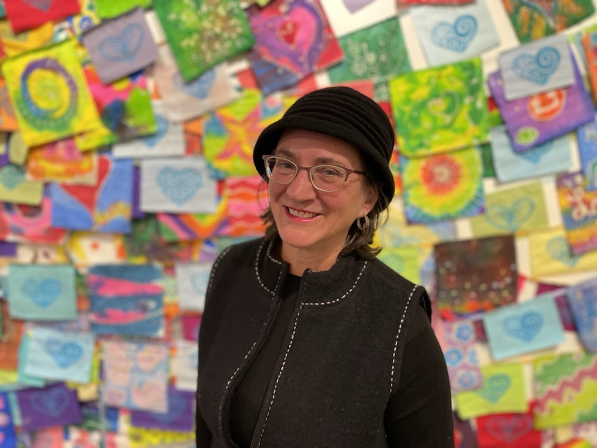 caption: Denise Henriksonstands in front of a wall of painted flags created during Ecothrive Housing's many listening sessions. The flags are currently on display at the Highline Heritage Museum
