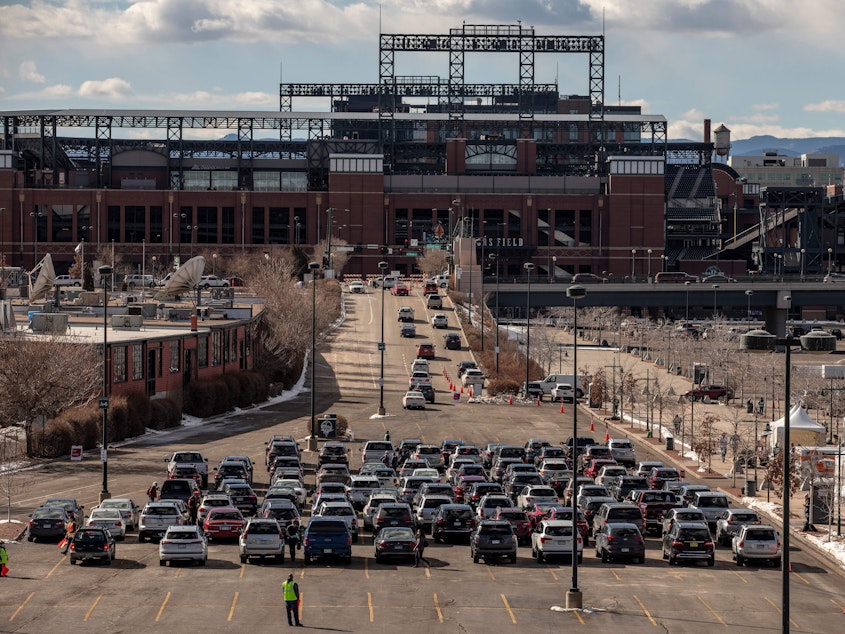 caption: People line up for drive-through COVID-19 vaccination at Coors Field baseball stadium in Denver on Saturday.