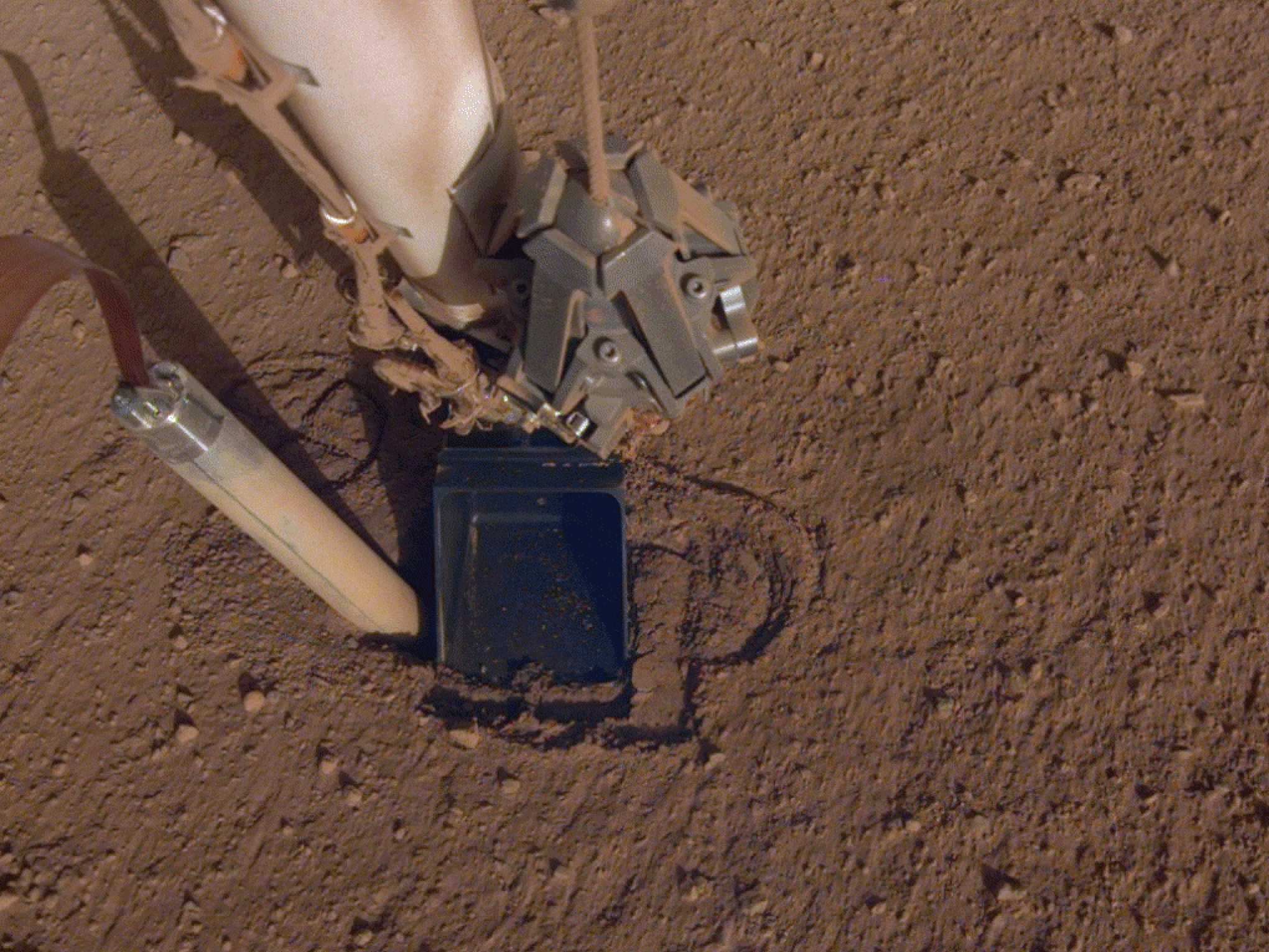 caption: A photo of the mole on NASA's InSight lander trying to drill into the Martian surface.
