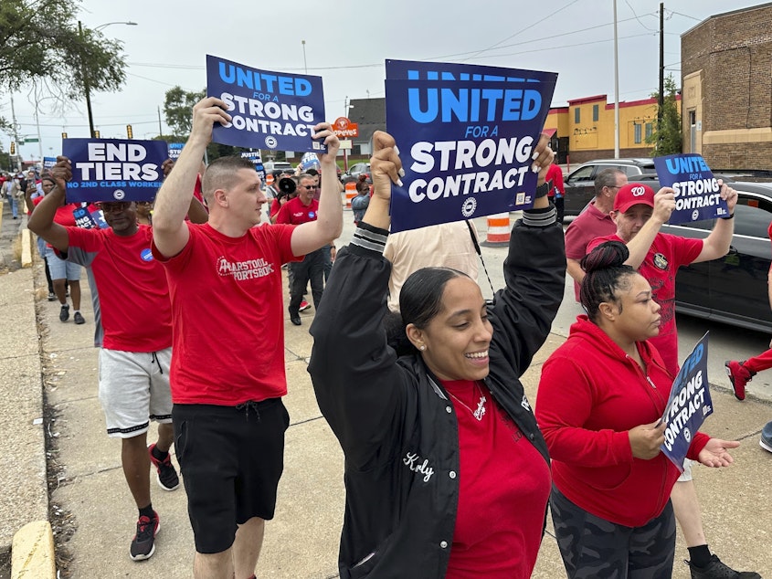 caption: United Auto Workers members march while holding signs at a union rally held near a Stellantis factory Wednesday, Aug. 23, 2023, in Detroit.