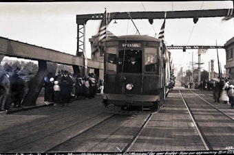 caption: A streetcar makes its way across Seattle's University Bridge in 1919. Behind the controls during this celebratory first crossing is the mayor, Ole Hanson.