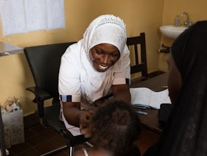 caption: Nabia Drammeh, 27, a nurse, talks with Maram Ceesay, and her granddaughter, Awa at the Brufut Minor Health Center outside of Banjul, the Gambia. Awa's mother passed away during childbirth leaving her Maram to look after her. The 2-year-old is being treated for pneumonia.