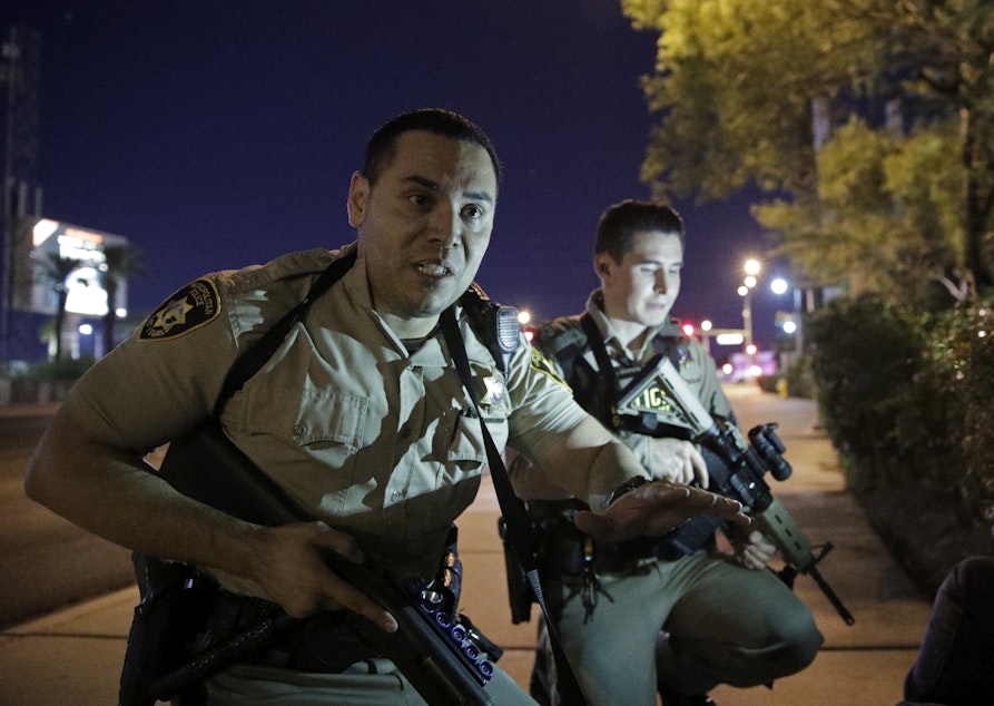 caption: Police officers advise people to take cover near the scene of a shooting near the Mandalay Bay resort and casino on the Las Vegas Strip, Sunday, Oct. 1, 2017, in Las Vegas.