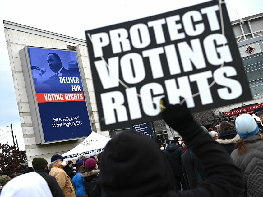 caption: A participant in the annual Martin Luther King Jr. Memorial Peace Walk in Washington, D.C., holds a sign that says "PROTECT VOTING RIGHTS" in 2022.