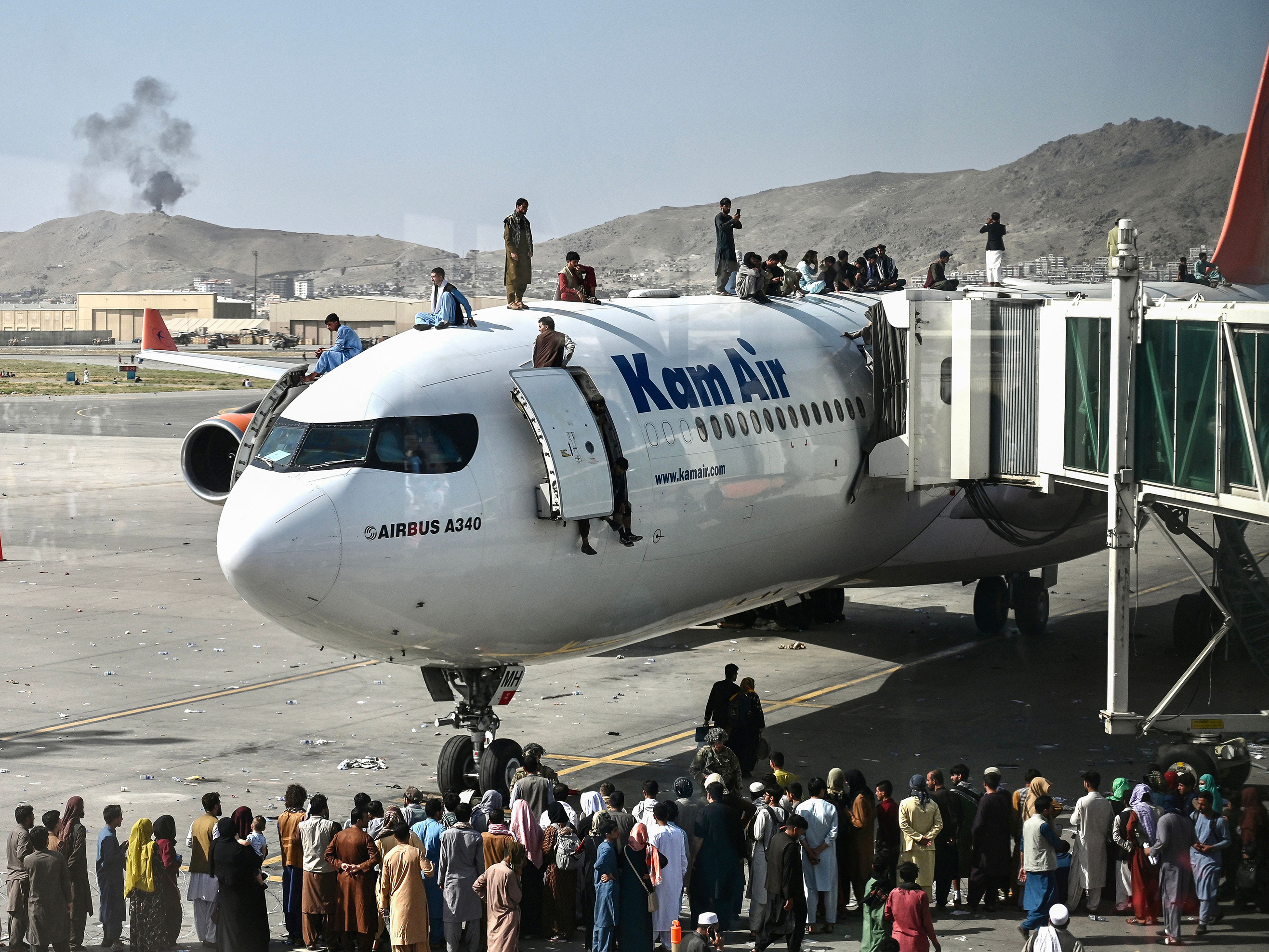 caption: Afghan people climb atop a plane as they wait at the Kabul airport in Kabul on Aug. 16, 2021, after a stunningly swift end to Afghanistan's 20-year war, as thousands of people mobbed the city's airport trying to flee the group's feared hardline brand of Islamist rule.