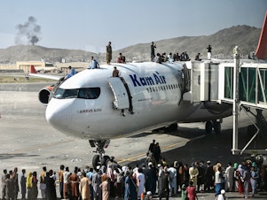 caption: Afghan people climb atop a plane as they wait at the Kabul airport in Kabul on Aug. 16, 2021, after a stunningly swift end to Afghanistan's 20-year war, as thousands of people mobbed the city's airport trying to flee the group's feared hardline brand of Islamist rule.
