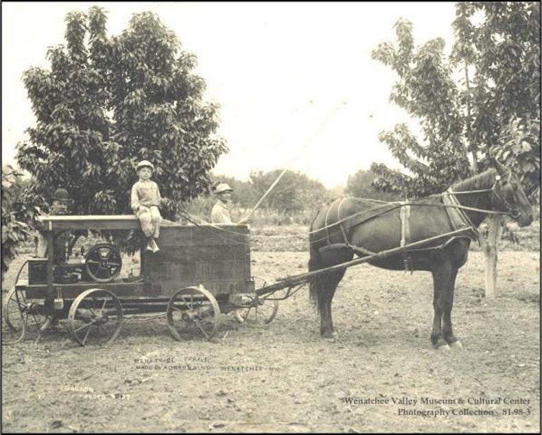 caption: A Wenatchee sprayer made by A. D. Browning, Wenatchee. Two men, one with bamboo spray pole, and one small boy sitting on top of sprayer pulled by one horse in a fruit orchard in Wenatchee.