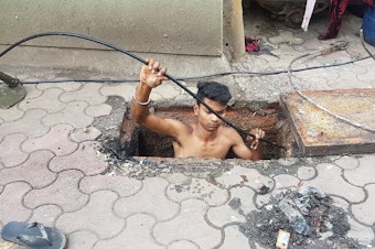 caption: Jitesh Singolia, 19, climbs down a manhole to clean sewer pipes using his bare hands.