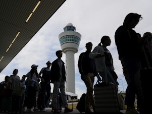caption: Travelers wait in long lines outside the terminal building to check in and board flights at Amsterdam's Schiphol Airport, Netherlands, Tuesday, June 21, 2022.