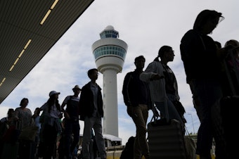 caption: Travelers wait in long lines outside the terminal building to check in and board flights at Amsterdam's Schiphol Airport, Netherlands, Tuesday, June 21, 2022.