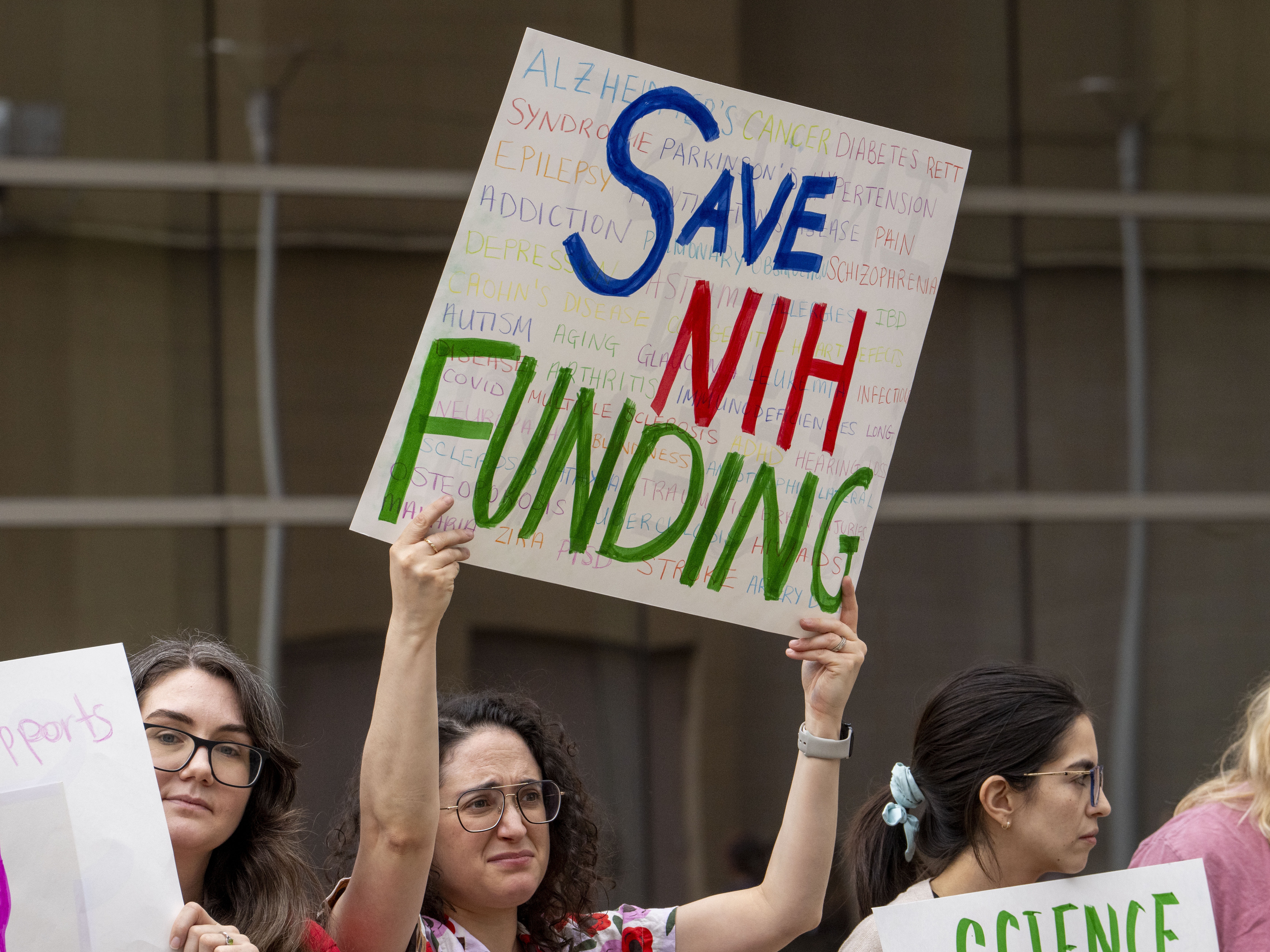 caption: A protestor in Houston, Texas, holds a sign in favor of funding from the National Institutes of Health on March 7 during a "Stand Up for Science" rally at the Houston Medical Center.
